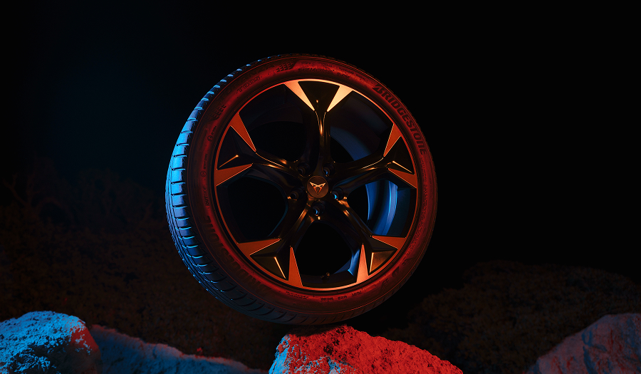 CUPRA Felge mit Reifen in Nahaufnahme, beleuchtet mit blauem und rotem Licht vor dunklem Hintergrund.